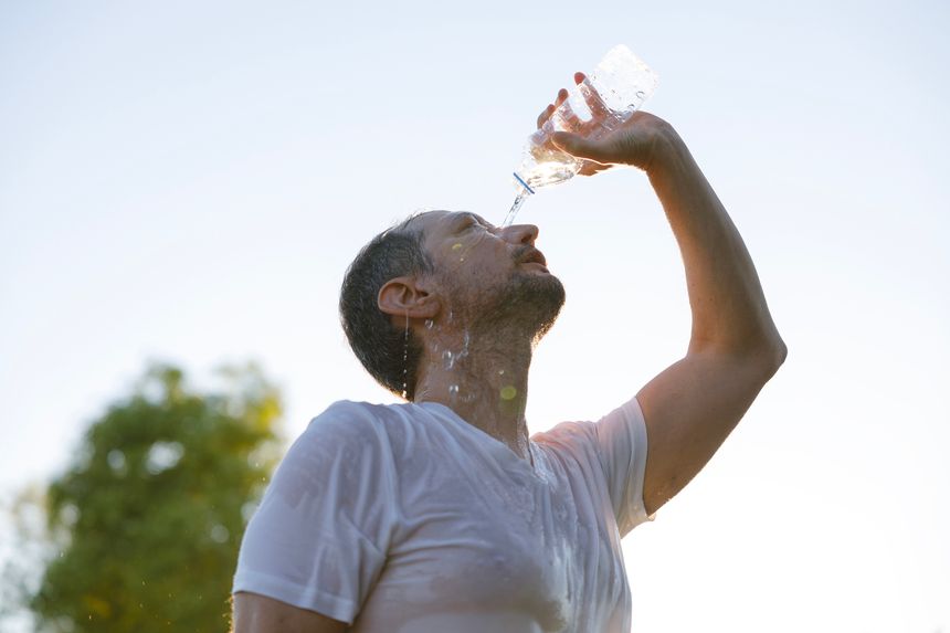 The young man, suffering from the extreme heat on a hot summer day, pours water on himself in the park