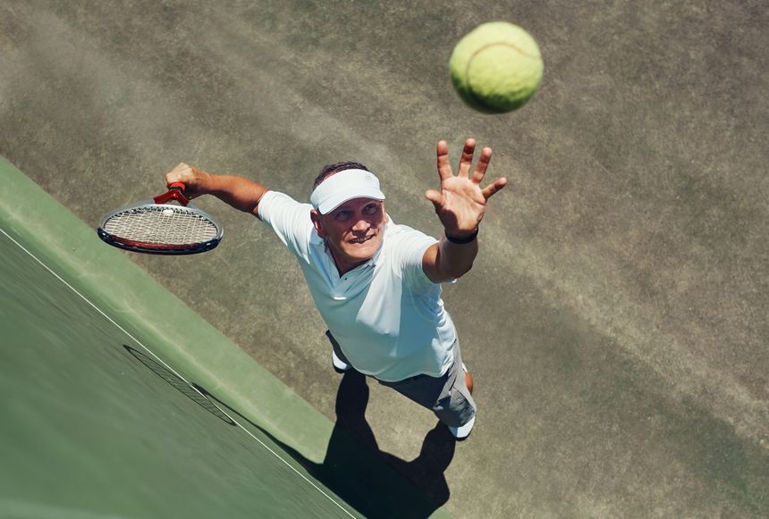 High angle shot of a focused middle aged man playing tennis while about to serve the ball to his opponent outside during the day
