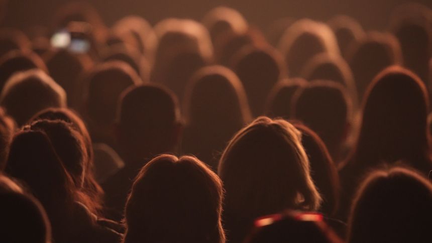 Many people in dark wait show start. Spectator ready watch epic film. Movie theater atmosphere. Fun teen audience before beginning. Joy cinema fans crowd sit at music concert hall. Orange night light.