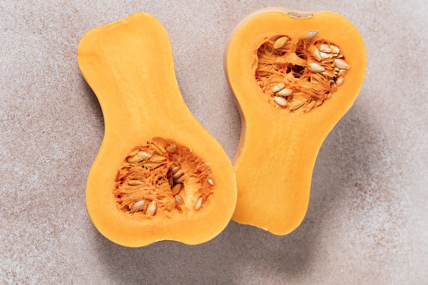 Butternut squash is halved, exposing the seeds and soft flesh. The light colored surface adds to the kitchen atmosphere. Fresh vegetables are ready for cooking.