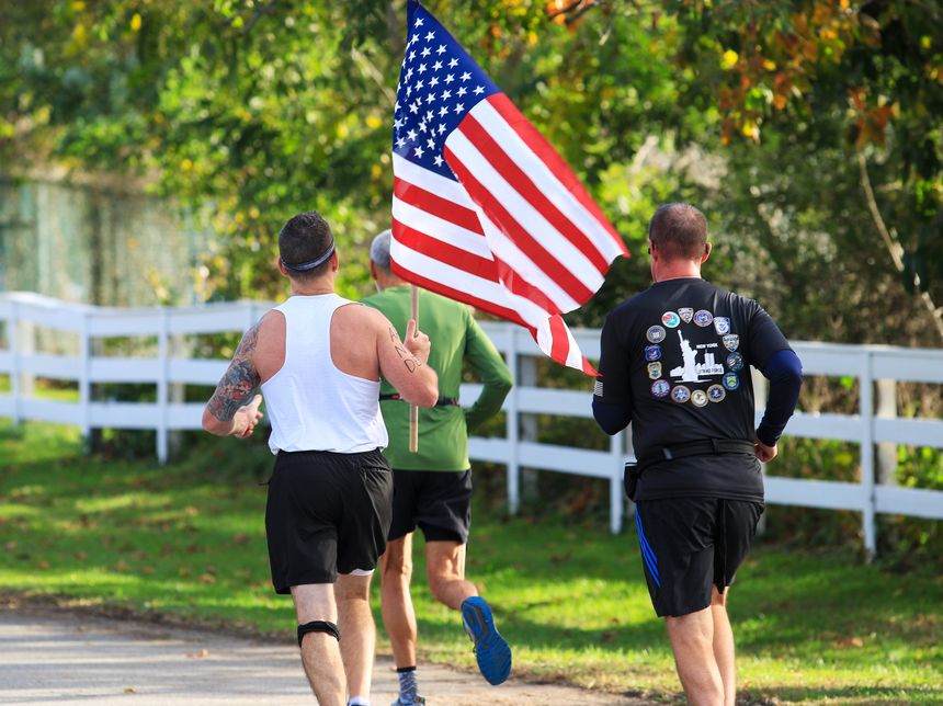 Bay Shore, New York, USA - 22 October 2023: Rear view of a man carrying an American flag during a road running race.
