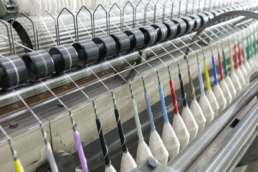 Closeup of warp yarn threads guided through loom system, illustrating precision textile weaving process for fabric manufacturing and industrial marketing use.