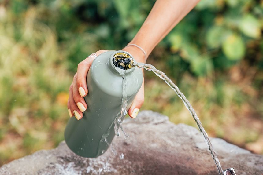 Woman filling her reusable water bottle at a public drinking fountain, promoting hydration and sustainability