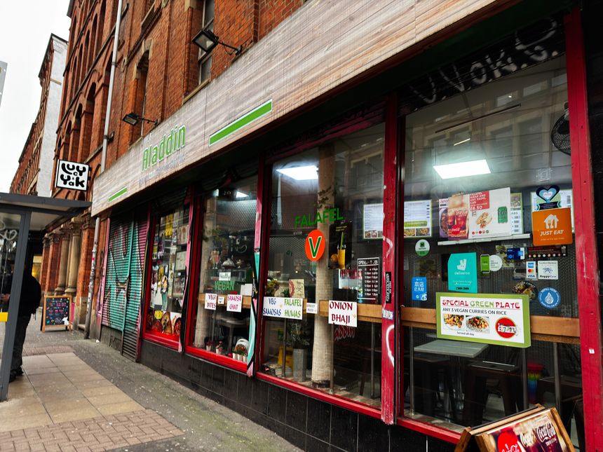 Manchester, UK - January 30, 2026: Vibrant street view of Little Aladdin vegan restaurant with colorful menus, signs, and urban shopfront Manchester