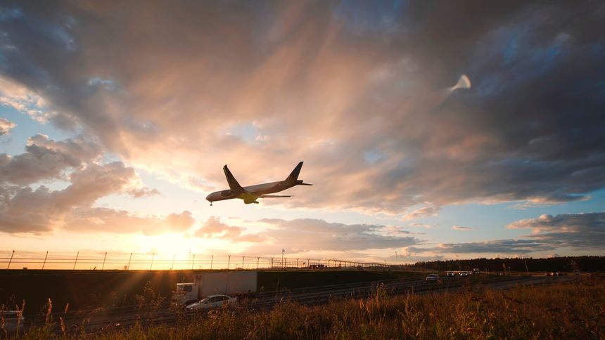 Wide-body passenger jet landing at sunset over highway traffic near airport