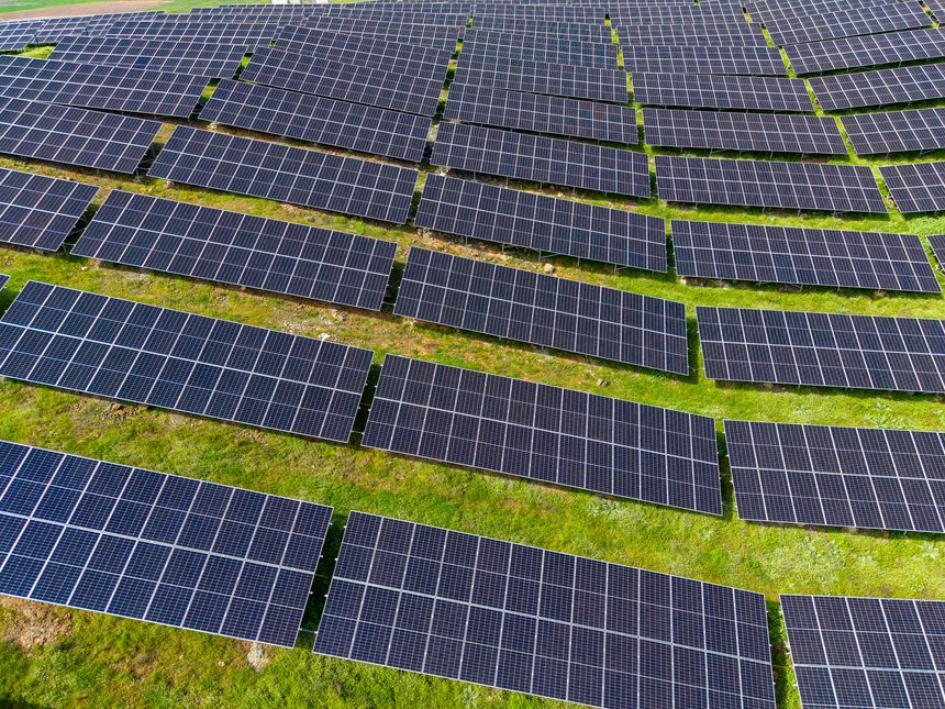 Rows of solar panels are installed on the ground in an open field. Sunlight shines on the panels, indicating they are gathering solar energy for power generation.