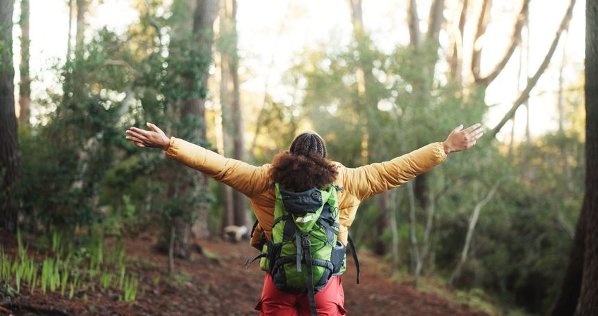 Woman, open arms and back with success for hiking, achievement and goals on adventure in forest. Person, celebration and bag with cheers in woods with winning, target and freedom on trail