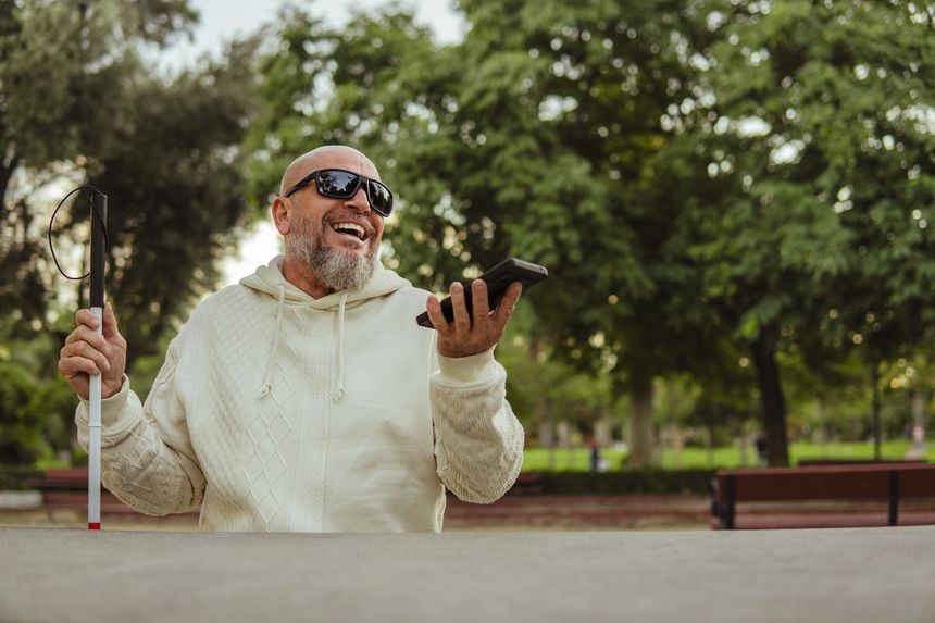Smiling Blind Man Talking on Hands-Free Mobile Phone Sitting in Park with Sunglasses and Walking Stick