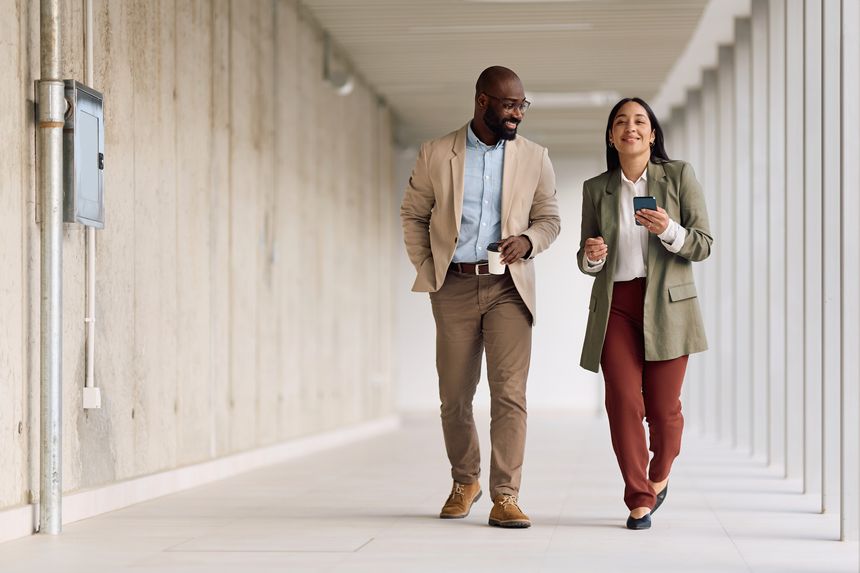 Happy African American businessman and his female colleague walking through a hallway in the office. Copy space.