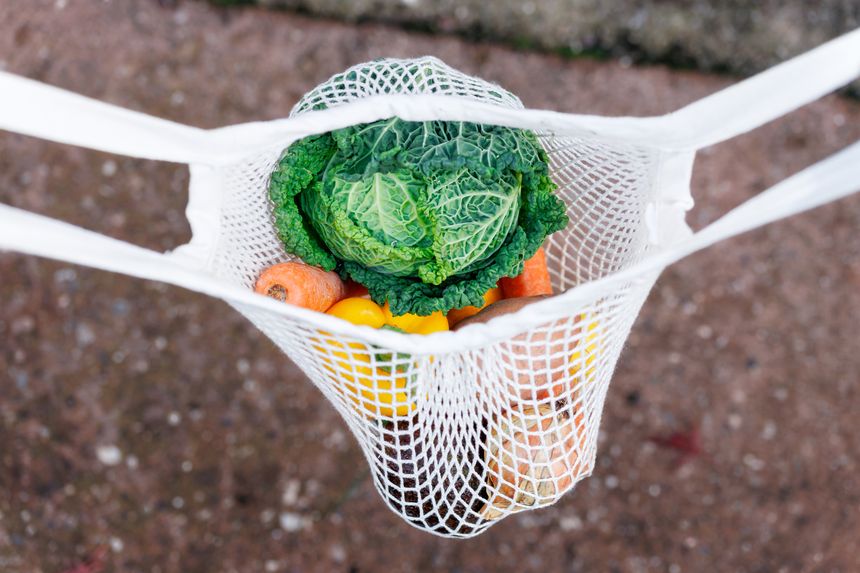 Woman Holding reusable Mesh grocery shopping Bag with Fresh Vegetables and fruits. Eco-friendly bag filled with fresh produce held by a person.