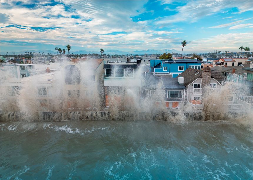 Large waves crash against oceanfront homes during heavy surf, sending spray above seawalls and highlighting the risks of coastal flooding, erosion, and storm-driven wave action in densely developed shoreline communities.