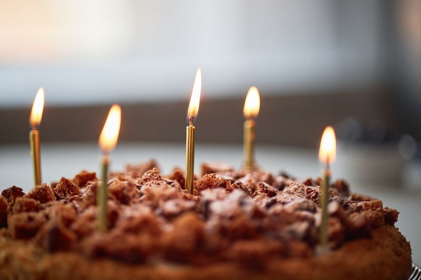 Chocolate cake with five lit candles standing on top, celebrating birthday or special occasion, close up of dessert with blurred background, no people visible in frame