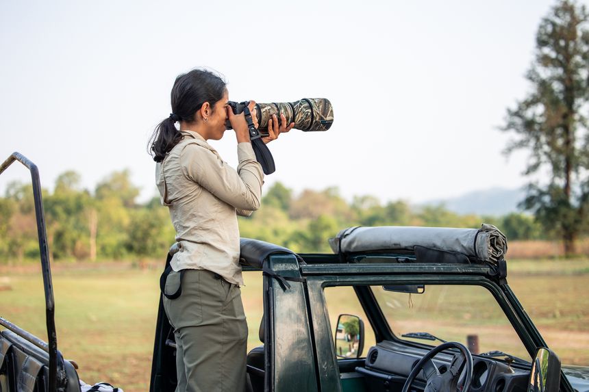 Young woman wildlife photographer capturing stunning images while standing on a jeep during an adventurous safari in the vibrant Indian jungle, surrounded by lush nature and wildlife