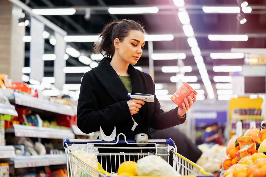 Young attractive woman holding bar code scanner and scanning products in store. Concept of modern gadgets and devices, Fruits and vegetables department. Healthy lifestyle. loosing weight.