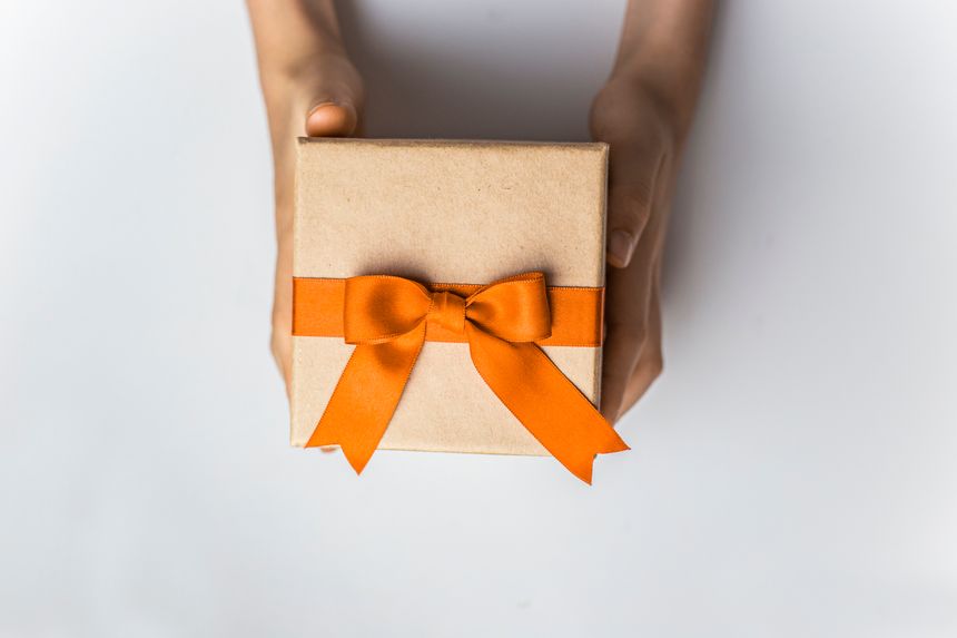 Cartboard gift box with orange ribbon and bow in hands on white background isolated