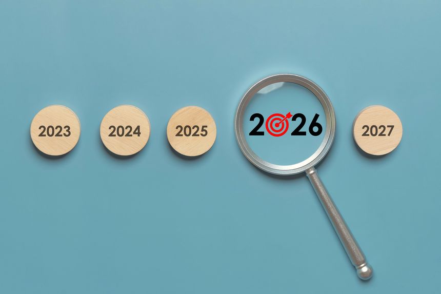 Magnifying glass highlighting 2026 target on wooden year circles 2023 to 2027 on blue background, New Year goals, annual planning, OKR, KPI, action plans, strategy, timeline, forecasting, and growth.