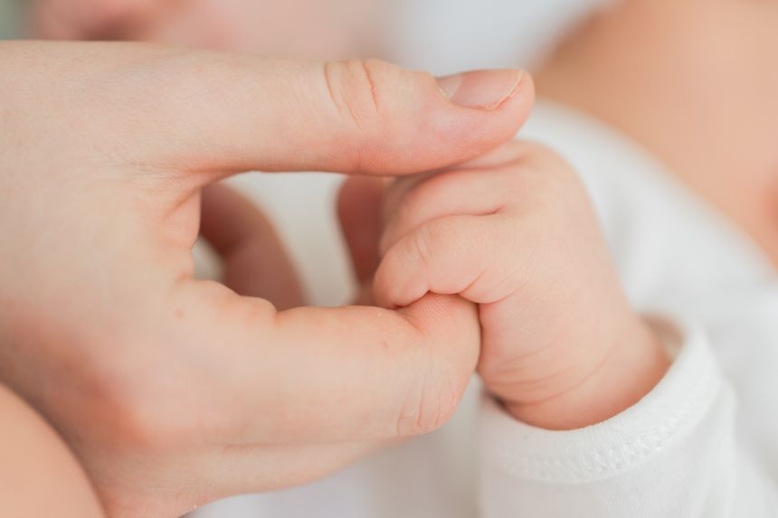Happy family. Tiny newborn infant baby little hand on mother hand palm. Newborn baby holding parent finger after birth. Mom baby at home. Support protection of new life. Handle with care