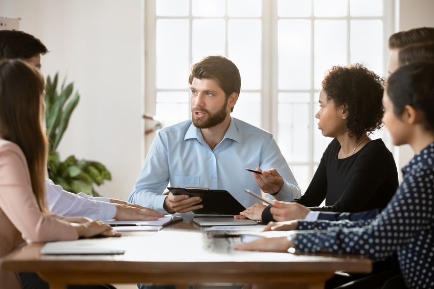 Serious skilled teammates gathered together at conference table for decision making, planning strategy, forecasting. Millennial team leader speaking during briefing event with corporate staff members