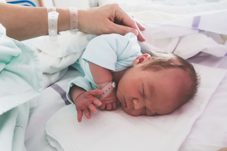 Mother and newborn resting after childbirth in maternity hospital room. Mother hugging her sleeping newborn baby.