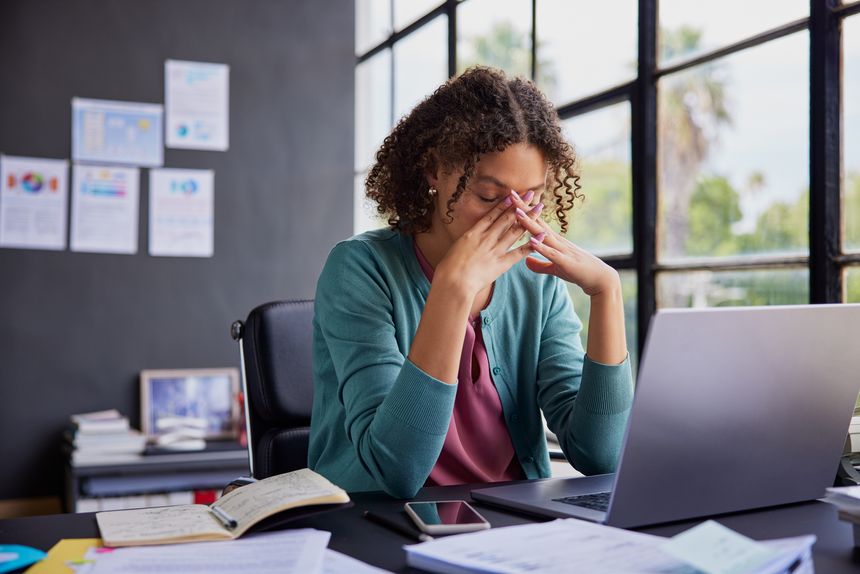 Exhausted businesswoman feeling stressed, holding her head while working on a laptop. Professional african american woman has terrible migraine while managing tasks in office with copy space. Overwhelmed businesswoman feeling tired and frustrated after read a bad news on financial market, overworked and burnout concept.