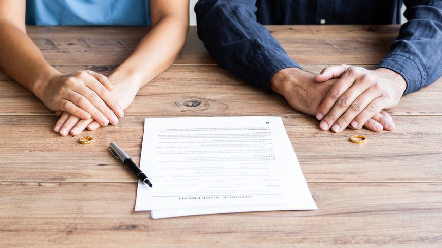Human hand signing divorce contract, close-up. Wedding rings with marriage contract and judge gavel on a background