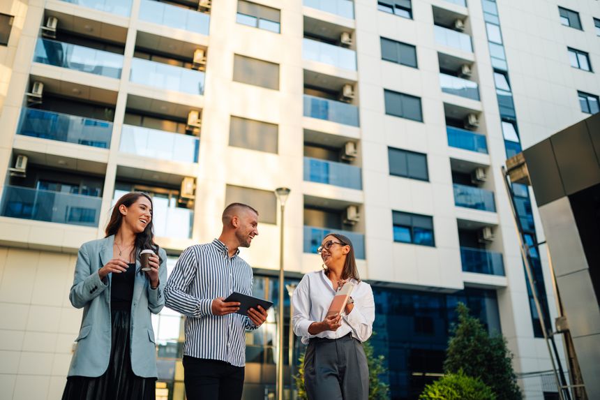 Three businesspeople are having a discussion outside on a break, holding coffee and a digital tablet while strategizing about their next sale