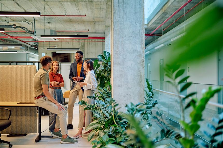 Group of diverse businesspeople engaged in a project discussion within a modern office filled with lush plants, fostering collaboration and creativity