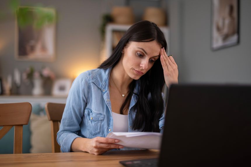 Young adult woman feeling frustrated and stressed while reviewing paperwork and bills