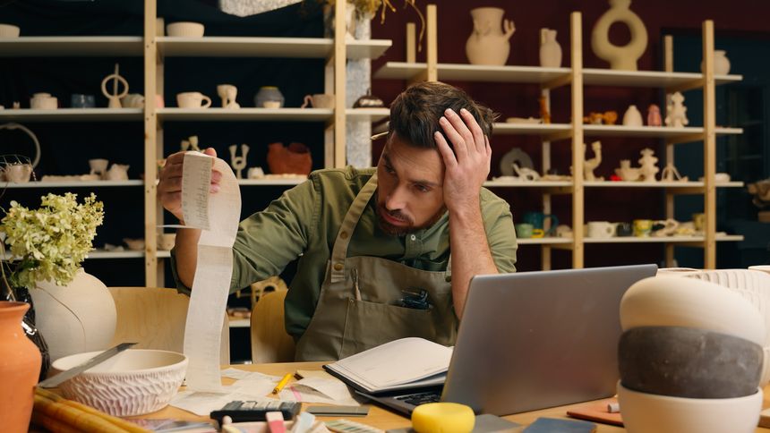 Shocked frustrated Caucasian man male small business owner potter gut businessman examining large bill check receipt debt bankruptcy shock payment problem unpaid tax accounting laptop in pottery store. High quality 4k footage