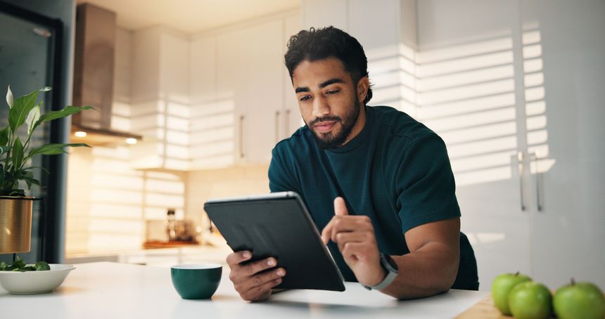 Tablet, coffee and man in kitchen in morning with networking, communication or app. Digital technology, research and male person with cappuccino for texting, contact or social media in apartment.