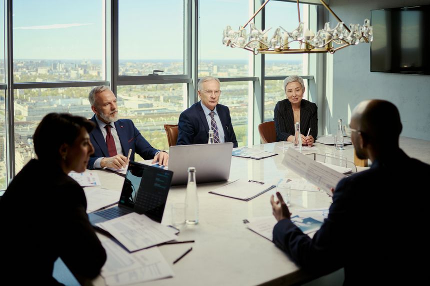 Wide shot of middle aged business team discussing strategy during oil industry meeting in boardroom, reviewing reports and laptop. Ideal for energy leadership, corporate planning, investment