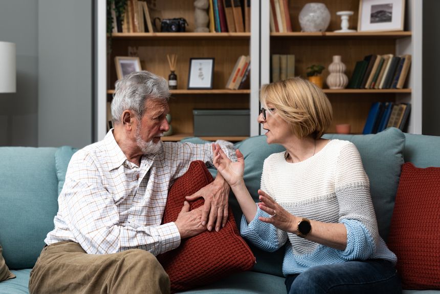 Irritated middle-age or senior couple has hard debate at home, sitting on the sofa and arguing, annoyed woman talking to angry man, mature spouses has problems in marriage and respect