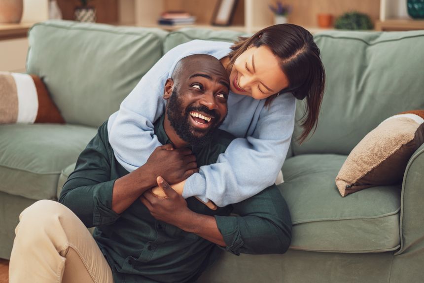 A cheerful interracial couple shares a joyful moment of laughter while relaxing at home.