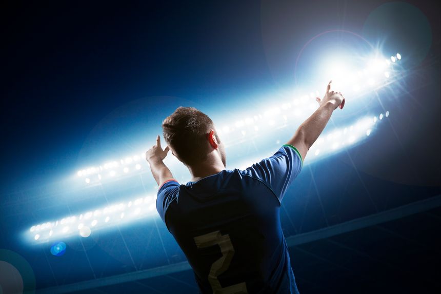 Soccer player with arms raised cheering, stadium at night time