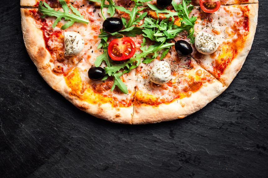 Pizza with tomatoes, mozzarella cheese and arugula. Pizza menu.Top view with copy space on dark stone table