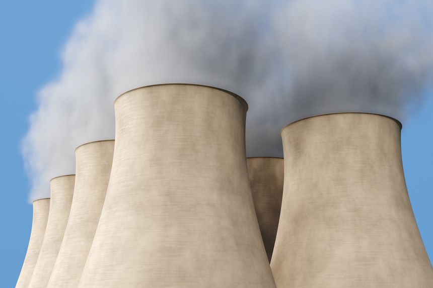 Cluster of cooling towers of a nuclear power plant emitting smoke under blue sky. Illustration of the concept of energy crisis, nuclear fission and clean energy