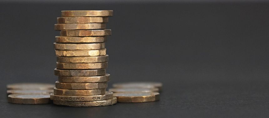 Pile, heap or stack of one and two pound sterling coins. Glowing in a golden light against a dark background. Metaphor for saving, investment, finance and wealth.