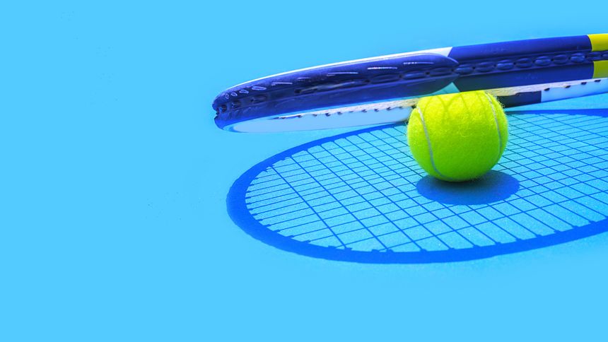 Summer sport concept with tennis ball and racket on blue hard tennis court. Top view, copy space.