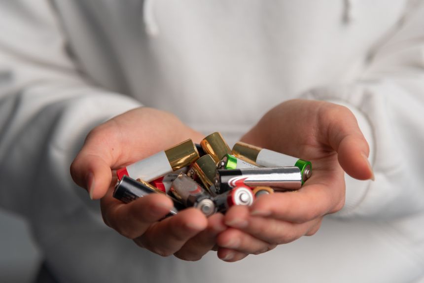 close up view of hands full of alkaline batteries, hands of young caucasian girl, white sweater in background, disposal of chemical current sources