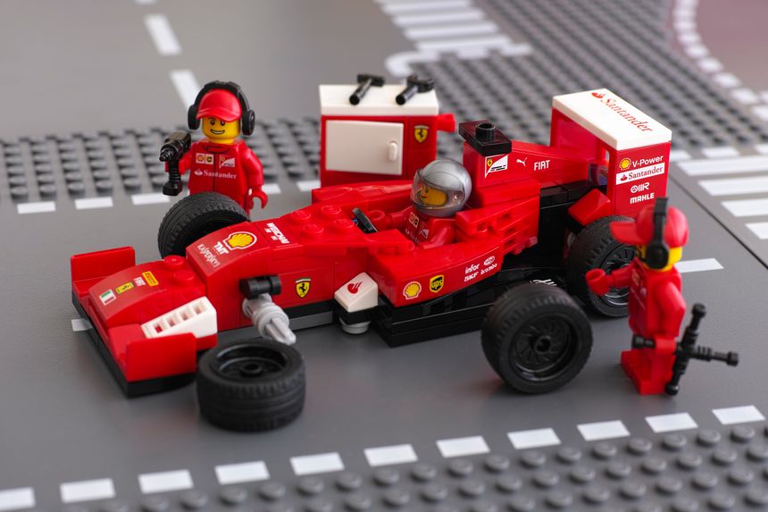 Tambov, Russian Federation - June 23, 2015: Lego team crew members are fixing wheel of Ferrari F14 T race car by LEGO Speed Champions on the Lego road baseplates. Studio shot.