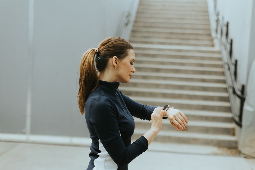 Focused individual monitors her smartwatch while preparing for an energetic morning run near a stylish staircase in an urban environment.