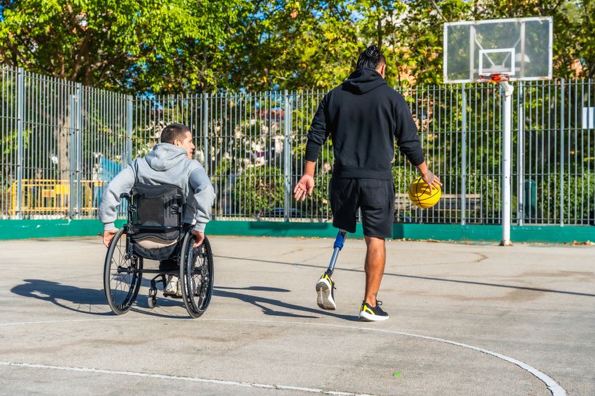 Two young adult friends with disabilities enjoying a game of basketball on an outdoor court, promoting concepts of inclusion, friendship, and adaptive sports