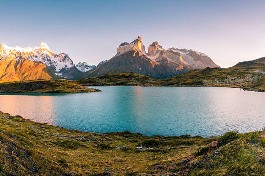Majestic mountain peaks and a serene turquoise lake at sunrise, surrounded by lush greenery and dramatic landscapes, inspire awe and tranquility, setting a scene of natural beauty and adventure.
