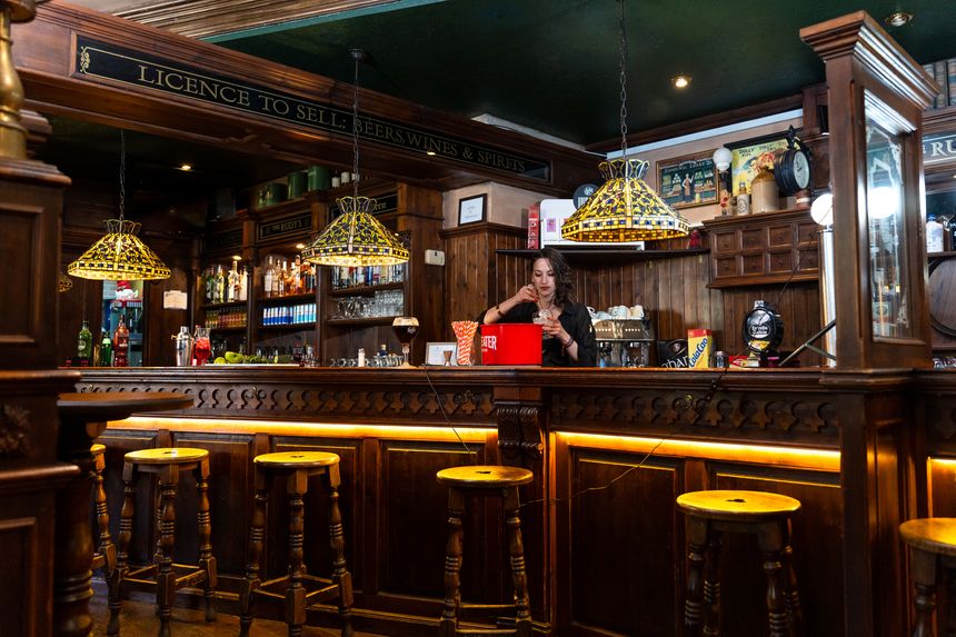 Female bartender mixing cocktails in a classic irish pub, surrounded by warm light, creating a cozy atmosphere for evening relaxation