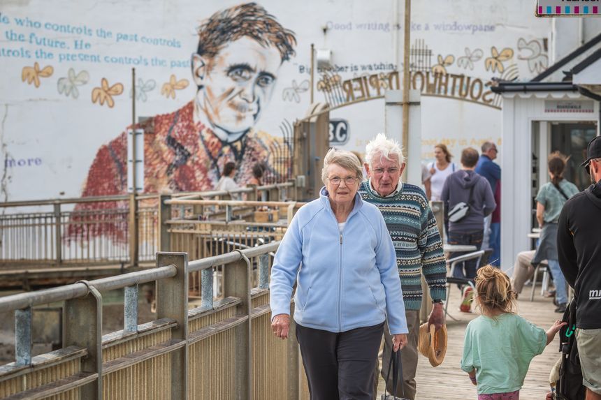 Southwold, UK - 26 August, 2025 - Two seniors walking on the Southwold Pier with a mural of the author George Orwell in the background