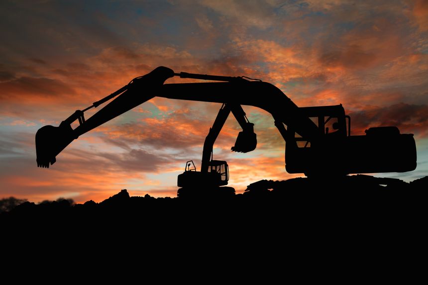 Two Crawler excavators silhouette are digging the soil in the construction site on sky of sunset background.