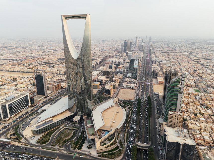 The drone gracefully soars over Riyadh, Saudi Arabia, capturing the majestic Kingdom Tower in the radiant daylight. Sunrise. The city sprawls beneath, reflecting modernity in its architecture, while the towering landmark stands as a beacon of progress. The image encapsulates Riyadh's vibrant spirit in the bright embrace of the sun. High quality 4k footage