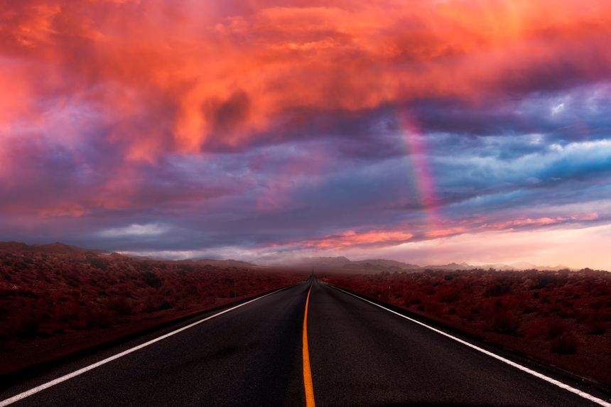 Dramatic sunset sky with stormy clouds and rainbow above route US 93 Alt in Nevada near Wendover with mountain peaks covered by rainy clouds.