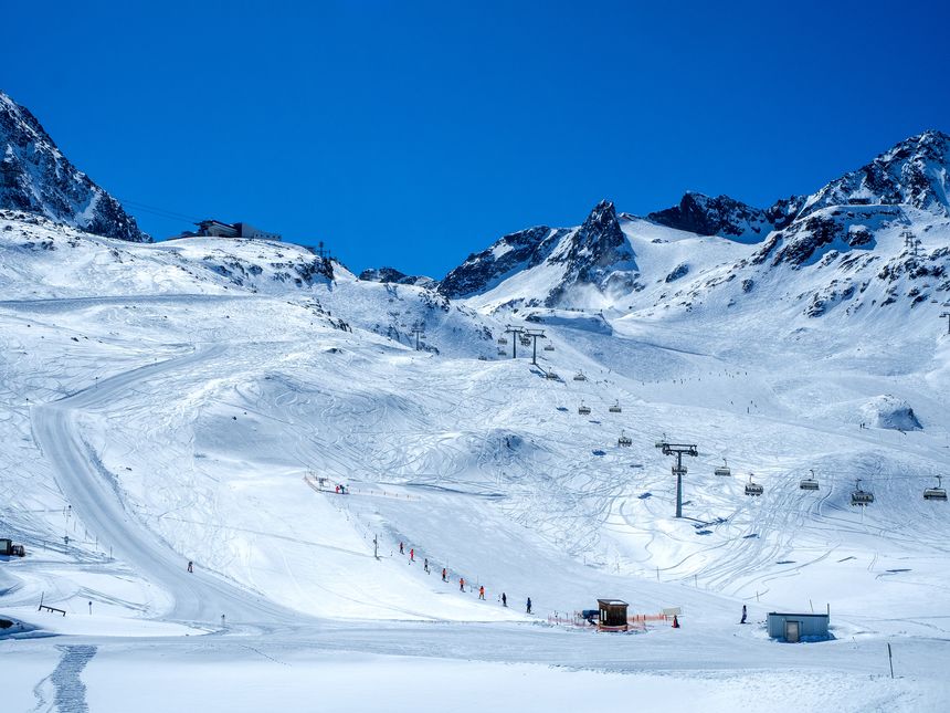 Stubai glacier in Austrian Alps with ski slopes, chairlifts, button lift, cable car upper station, skiers and snowboarders. Blue sky with copy space