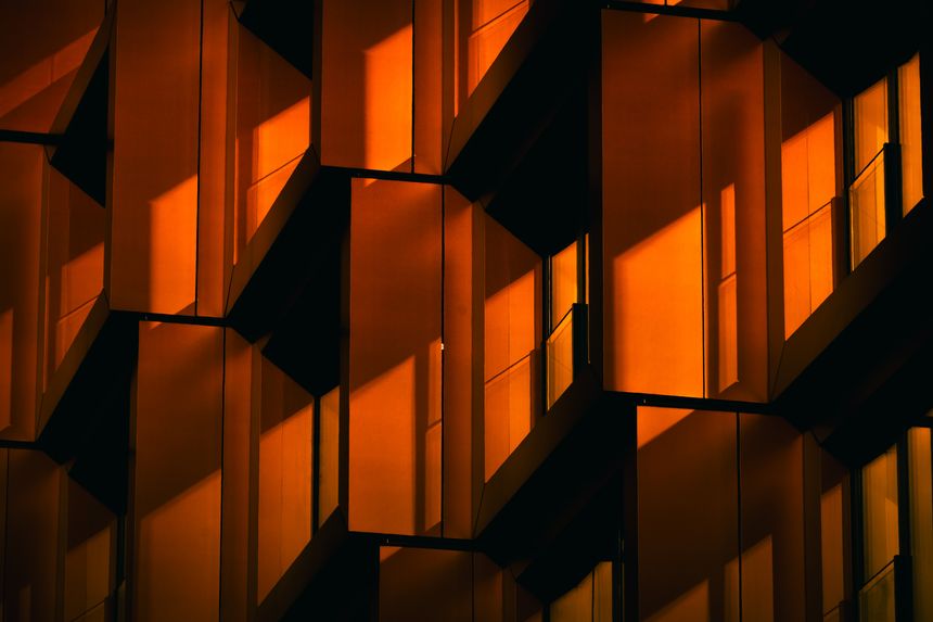 Modern residential facade with stacked orange balconies casting strong geometric shadows, modern residential complex